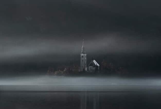 A panoramic view of a desolate, fog-covered landscape, with a dark and ominous-looking abandoned building in the distance. The sky is overcast, and the overall mood is bleak and unsettling.